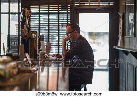 Stock Photo - Barman typing on laptop at public house counter. Fotosearch