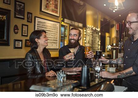 Bartender and young couple raising a toast in public house View Large Photo Image Picture - Bartender and young couple raising a toast in public house. Fotosearch