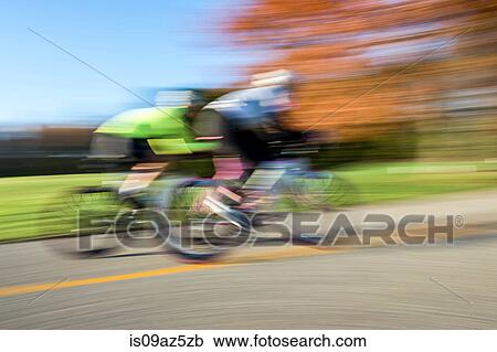 Stock Image - Blurred motion side view of cyclists cycling. Fotosearch