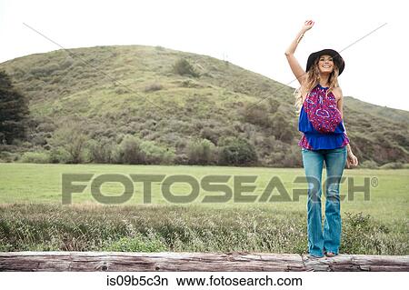 Picture - Boho style young woman waving from log. Fotosearch