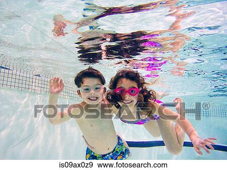 Boy and girl underwater in swimming pool wearing goggles looking at camera smiling View Large Photo Image Stock Photo - Boy and girl underwater in swimming pool wearing goggles looking at camera smiling. Fotosearch