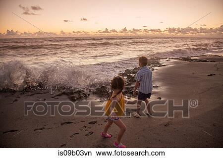 Boy and sister running away from splashing waves on beach at sunrise, Blowing Rocks Preserve, Jupiter Island, Florida, USA View Large Photo Image Picture - Boy and sister running away from splashing waves on beach at sunrise, Blowing Rocks Preserve, Jupiter Island, Florida, USA. Fotosearch