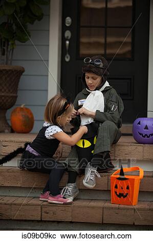 Stock Image - Boy and sister trick or treating in cat and pilot costume sitting on stairway looking in bags. Fotosearch