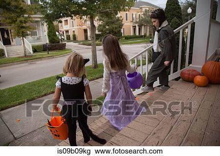 Stock Image - Boy and sisters trick or treating moving down porch stairway. Fotosearch