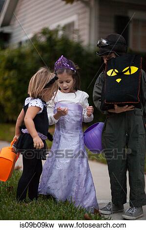 Boy and sisters trick or treating looking at treats on sidewalk View Large Photo Image Stock Photo - Boy and sisters trick or treating looking at treats on sidewalk. Fotosearch