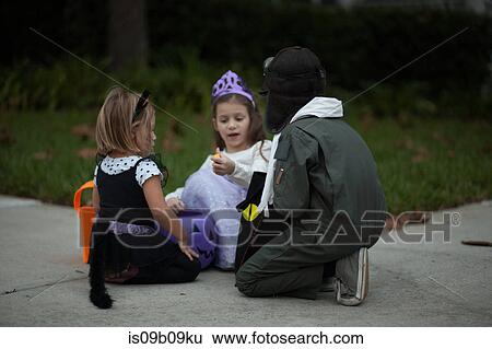 Boy and sisters trick or treating crouching and looking at treats on sidewalk View Large Photo Image Stock Photograph - Boy and sisters trick or treating crouching and looking at treats on sidewalk. Fotosearch