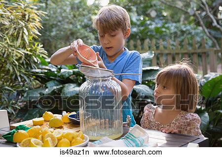 Boy and young sister pouring lemon juice for lemonade at garden table View Large Photo Image Picture - Boy and young sister pouring lemon juice for lemonade at garden table. Fotosearch