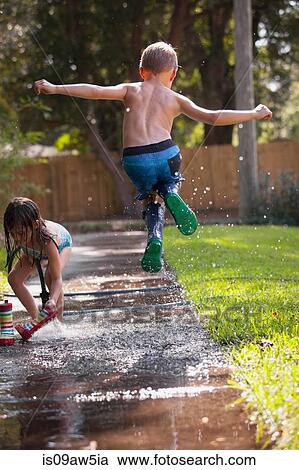 Stock Image - Boy in wellies jumping in mid-air on sidewalk. Fotosearch