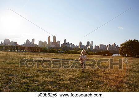 Stock Photograph - Boy running in park in front of New York skyline, USA. Fotosearch