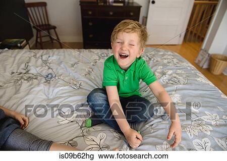 Stock Image - Boy sitting crosslegged on bed laughing. Fotosearch