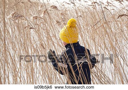 Stock Photograph - Boy walking through long grass, in snow covered landscape, rear view. Fotosearch