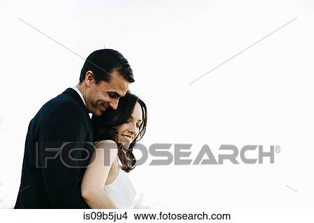 Picture - Bride and groom, outdoors, groom standing behind bride, smiling. Fotosearch