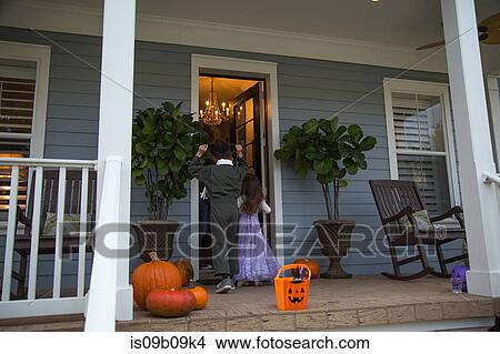 Picture - Brother and sister trick or treating at neighbour's front door. Fotosearch