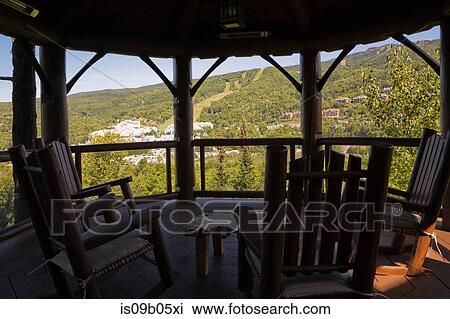 Stock Image - Brown gazebo and chairs on wooden deck with tempered glass and log railings at back of luxurious cottage style log home in summer, Quebec, Canada. Fotosearch