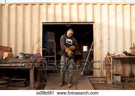 Stock Image - Builders in front of shipping container putting on protective gloves. Fotosearch