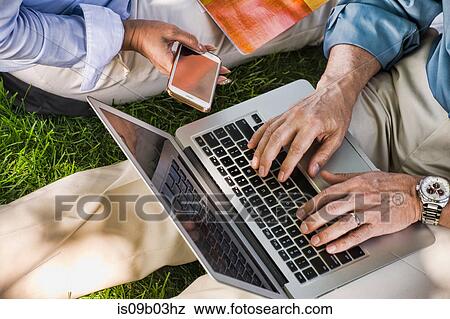 Business man and woman sitting outdoors on grass, using laptop, mid section View Large Photo Image Stock Photo - Business man and woman sitting outdoors on grass, using laptop, mid section. Fotosearch