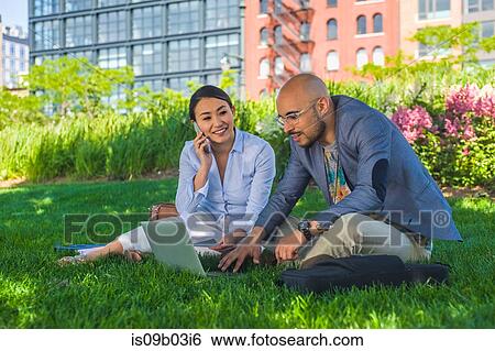 Businessman and woman sitting outdoors on grass, using laptop View Large Photo Image Stock Photograph - Businessman and woman sitting outdoors on grass, using laptop. Fotosearch