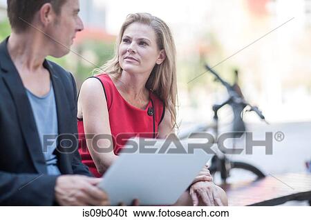 Stock Photograph - Businessman and woman using laptop and chatting in city park. Fotosearch