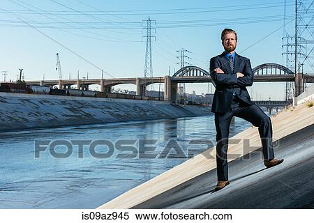 Stock Photography - Businessman arms crossed, looking at camera, Los Angeles river, California, USA. Fotosearch