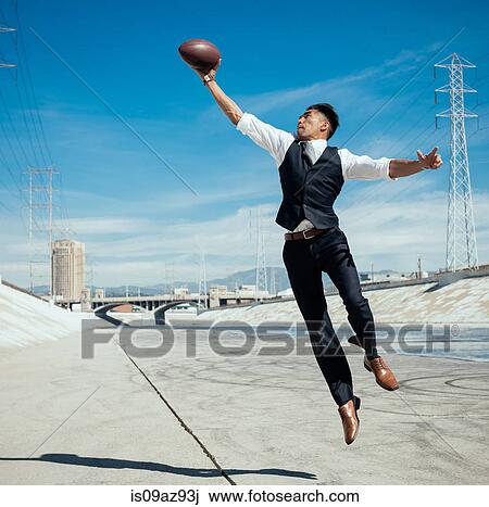 Stock Image - Businessman catching american football on Los Angeles river, California, USA. Fotosearch