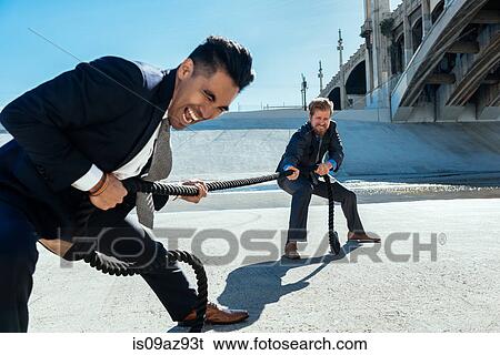 Stock Photograph - Businessman doing tug of war with rope, Los Angeles river, California, USA. Fotosearch