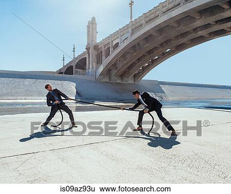 Stock Photograph - Businessman doing tug of war with rope, Los Angeles river, California, USA. Fotosearch