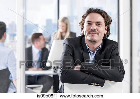 Businessman in office, colleagues chatting in background View Large Photo Image Stock Image - Businessman in office, colleagues chatting in background. Fotosearch