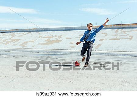 Stock Image - Businessman playing soccer on Los Angeles river, California, USA. Fotosearch