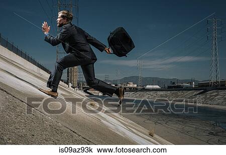 Stock Image - Businessman running up riverbank, Los Angeles river, California, USA. Fotosearch