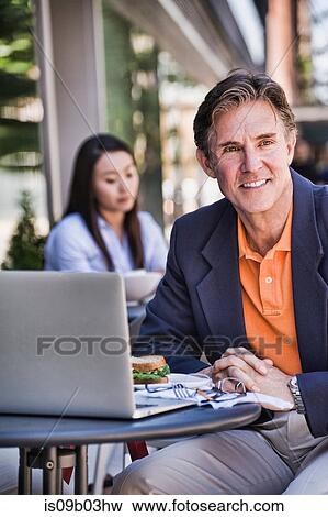 Stock Photo - Businessman sitting outside cafe, using laptop. Fotosearch