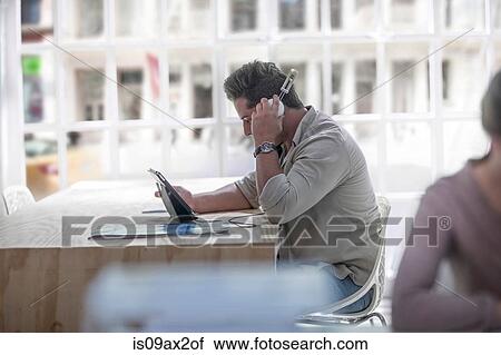 Businessman using digital tablet with headphones in loft office View Large Photo Image Stock Image - Businessman using digital tablet with headphones in loft office. Fotosearch