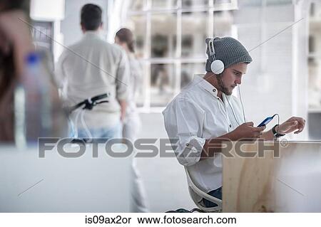 Businessman using smartphone with headphones in loft office View Large Photo Image Stock Photography - Businessman using smartphone with headphones in loft office. Fotosearch