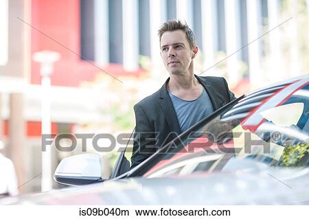 Businessman waiting next to car in city View Large Photo Image Picture - Businessman waiting next to car in city. Fotosearch