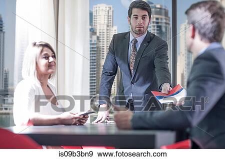 Businessmen and woman handing paperwork at meeting in conference room View Large Photo Image Stock Photo - Businessmen and woman handing paperwork at meeting in conference room. Fotosearch