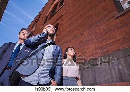 Businessmen and women walking outdoors, using smartphone, low angle view View Large Photo Image Stock Image - Businessmen and women walking outdoors, using smartphone, low angle view. Fotosearch