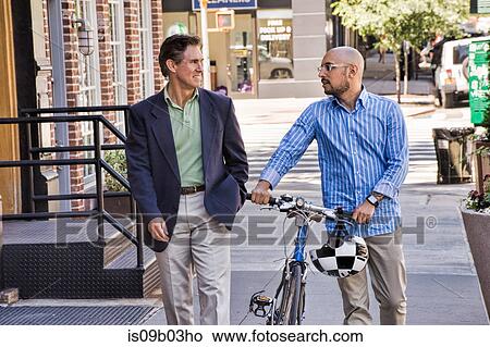 Businessmen walking in street, mid adult man pushing bike, smiling View Large Photo Image Picture - Businessmen walking in street, mid adult man pushing bike, smiling. Fotosearch