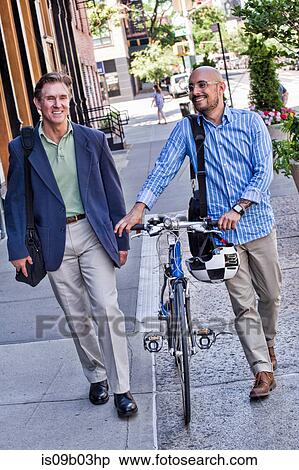 Stock Photography - Businessmen walking in street, mid adult man pushing bike, smiling. Fotosearch