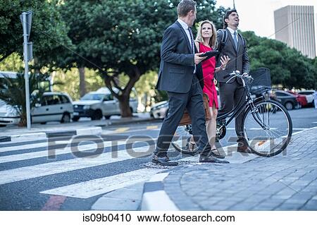 Stock Image - Businesswoman and male colleagues walking and talking in city. Fotosearch