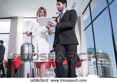 Stock Image - Businesswoman and man looking at digital tablet in hotel lobby. Fotosearch