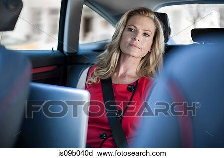 Stock Image - Businesswoman using laptop and looking from car back seat. Fotosearch