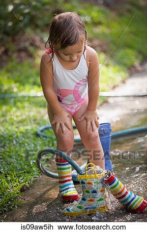 Stock Image - Child filling wellies with water from hose. Fotosearch