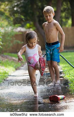 Stock Photo - Child in wellies playing in puddle of water, brother watching. Fotosearch