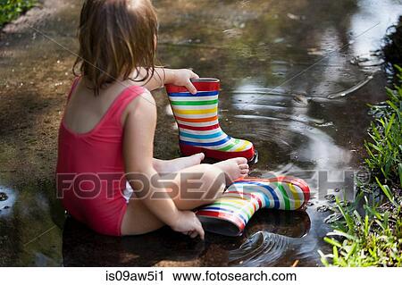 Child in wellies sitting in puddle of water View Large Photo Image Stock Image - Child in wellies sitting in puddle of water. Fotosearch