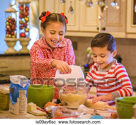 Stock Image - Children in kitchen wearing pyjamas using hand mixer on cookie dough smiling. Fotosearch