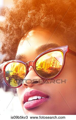 Stock Image - Close up portrait of young female fashion blogger with afro hair and mirrored sunglasses, New York, USA. Fotosearch