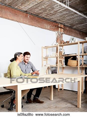 Colleagues at desk in workshop looking at laptop computer View Large Photo Image Picture - Colleagues at desk in workshop looking at laptop computer. Fotosearch