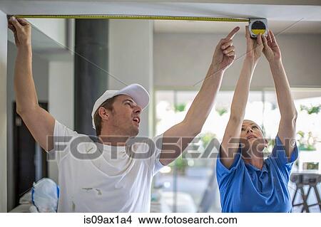 Picture - Couple, arms raised, using tape measure to measure ceiling. Fotosearch