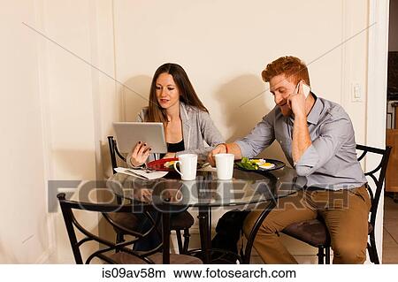 Couple at dining table using smartphone and digital tablet View Large Photo Image Picture - Couple at dining table using smartphone and digital tablet. Fotosearch