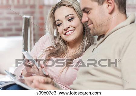 Couple at home, relaxing on sofa, looking at smartphone View Large Photo Image Stock Image - Couple at home, relaxing on sofa, looking at smartphone. Fotosearch