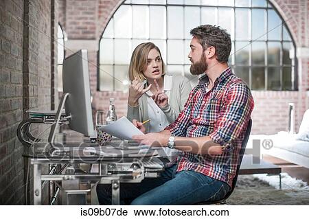 Couple at home, sitting at desk, using computer, having discussion, man holding paperwork View Large Photo Image Stock Image - Couple at home, sitting at desk, using computer, having discussion, man holding paperwork. Fotosearch